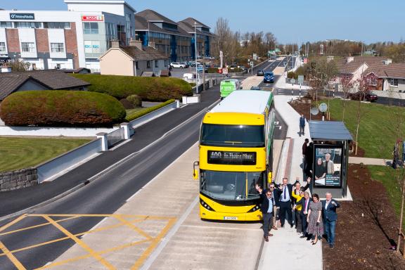 A drone shot of a group of people in front of a bus, at the opening of the project.