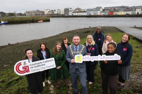 GCC Staff and Mayor standing at the Claddagh Basin holding up the Galway City Council Logo. The long walk is behind them.