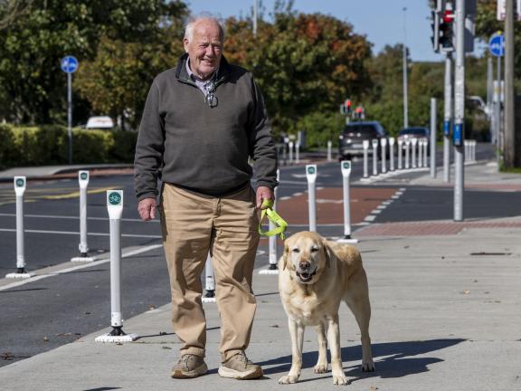 A man and a dog standing on a footpath beside a cycle lane, posing for the camera