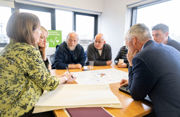 Group of people sitting at a table in a circle at a workshop in session in Ballybane