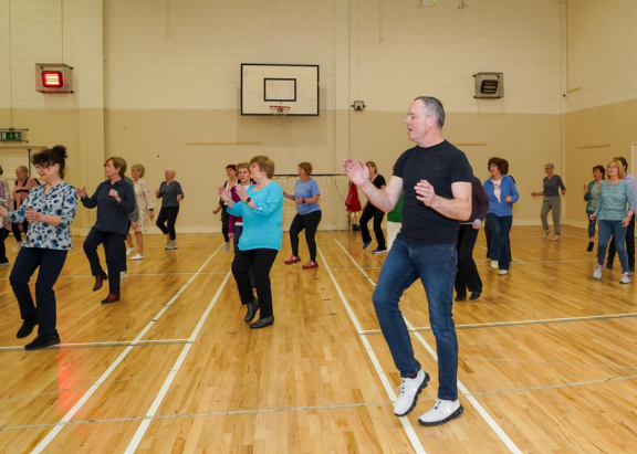 Dance class in session with a man to the foreground leading and clapping his hands