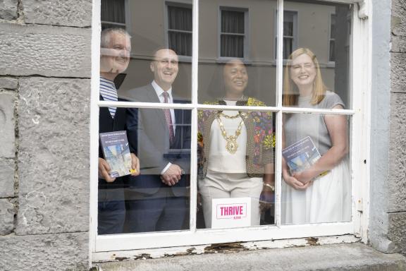 Staff behind the window of the Galway Arts Centre posing for photo holding the strategy leaflets