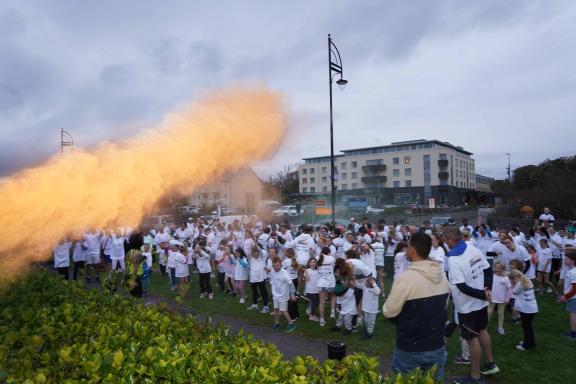 People lined up and dancing at Colour Run, flare of orange paint