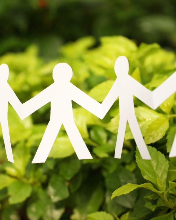 Paper men holding hands in front of greenery