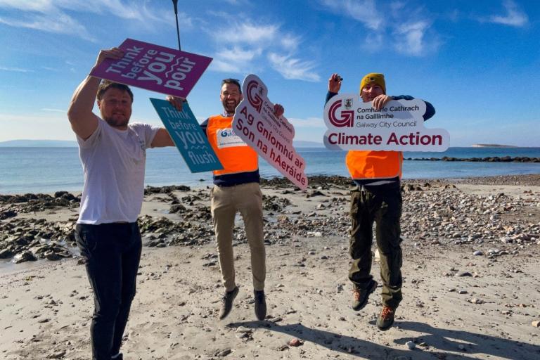 People jumping on a beach holding signs for Clean Coasts and GCC Climate Action