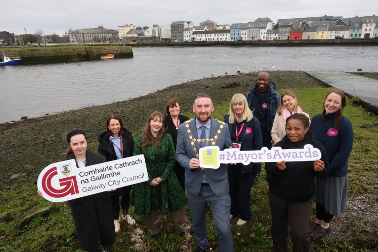 GCC Staff and Mayor standing at the Claddagh Basin holding up the Galway City Council Logo. The long walk is behind them.