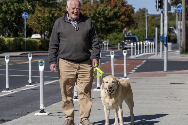 A man and a dog standing on a footpath beside a cycle lane, posing for the camera