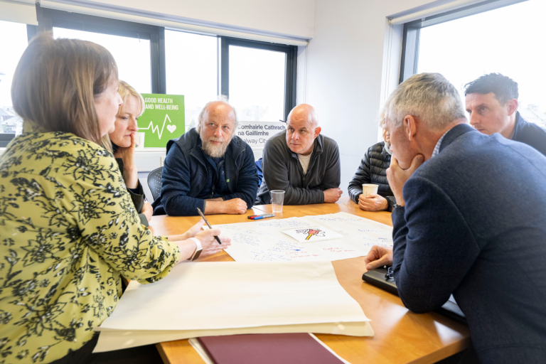 Group of people sitting at a table in a circle at a workshop in session in Ballybane
