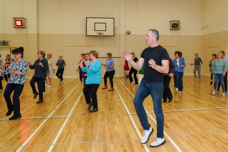 Dance class in session with a man to the foreground leading and clapping his hands