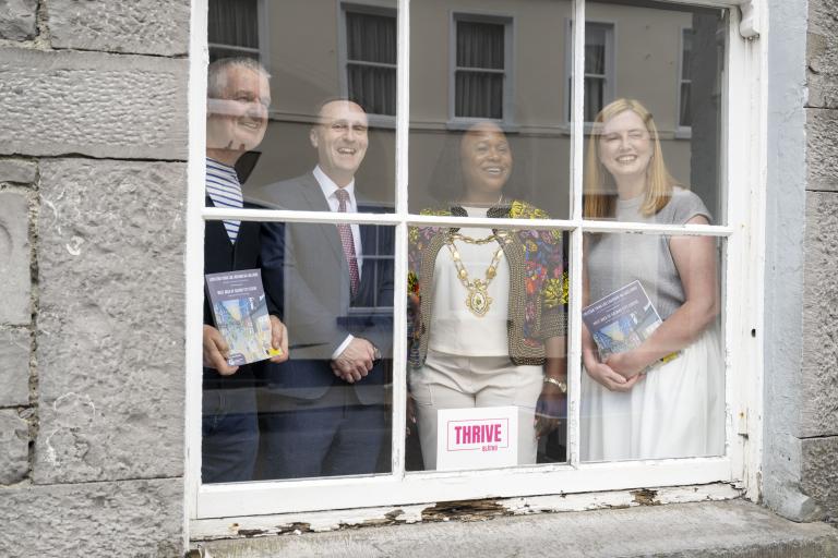 Staff behind the window of the Galway Arts Centre posing for photo holding the strategy leaflets