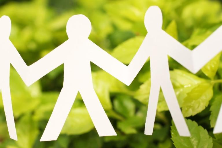 Paper men holding hands in front of greenery