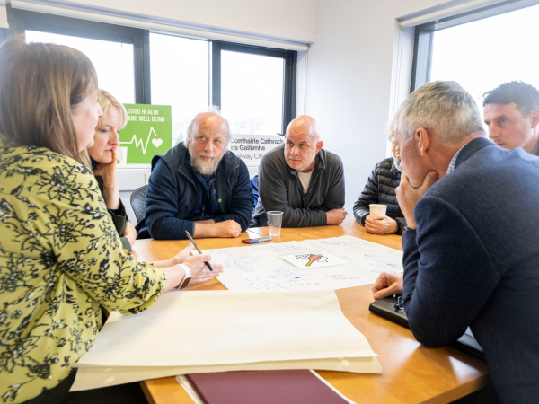 Group of people sitting at a table in a circle at a workshop in session in Ballybane