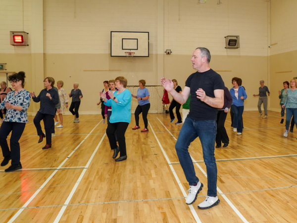 Dance class in session with a man to the foreground leading and clapping his hands